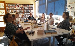 Osiem kobiet siedzi przy stole, na stole leżą książki