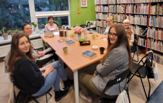 kobiety siedzą wokół stołu, na którym leżą książki
