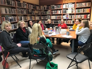 kobiety siedzą wokół stołu, na którym leżą książki