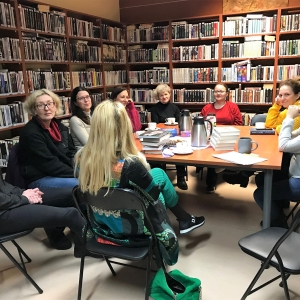 kobiety siedzą wokół stołu, na którym leżą książki