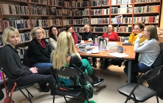 kobiety siedzą wokół stołu, na którym leżą książki