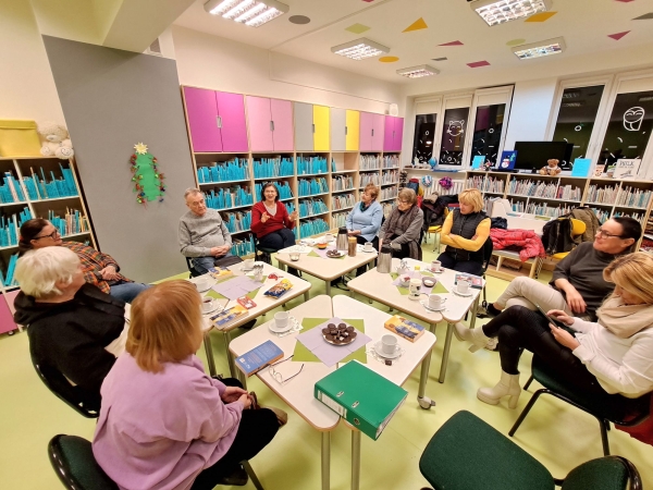 DKK Oddziału Czechowice- Niespokojni ludzie- styczeń_02 Osoby siedzące wkoło stołu w bibliotece przy książkach i kawie.