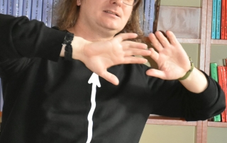 mężczyzna gestykuluje, w tle półki z książkami