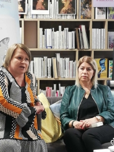 dwie kobiety siedzą na tle regałów bibliotecznych z książkami