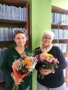 dwie kobiety z bukietem kwiatów stoją na tle regałów z książkami