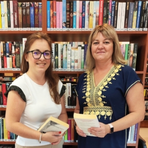 dwie kobiety stoją na tle regału z książkami