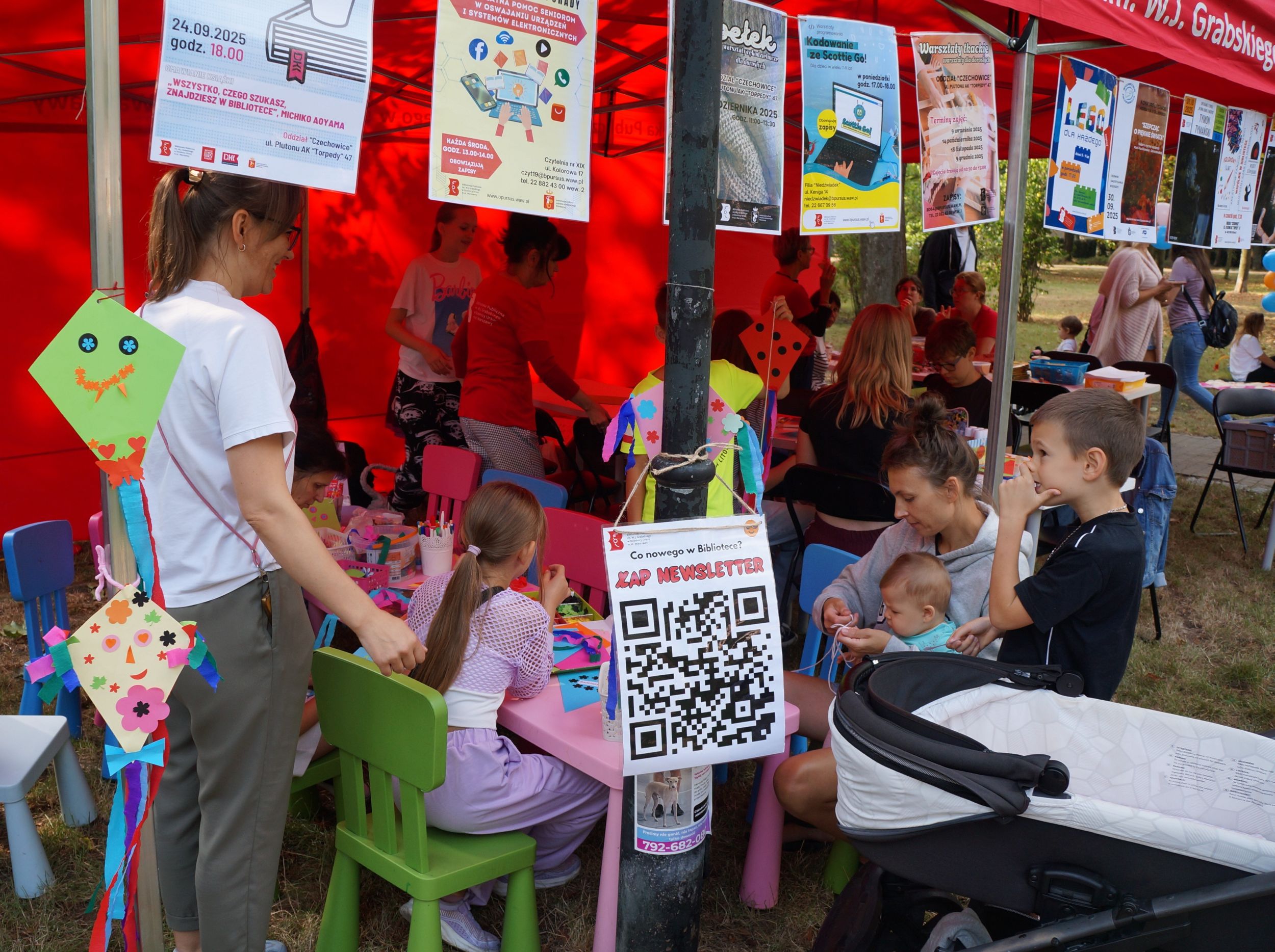DSC04052 Czerwony namiot Biblioteki Publicznej w Ursusie, pod którym odbywają się zajęcia dla dzieci. Przed namiotem idą uśmiechnięte uczestniczki wydarzenia