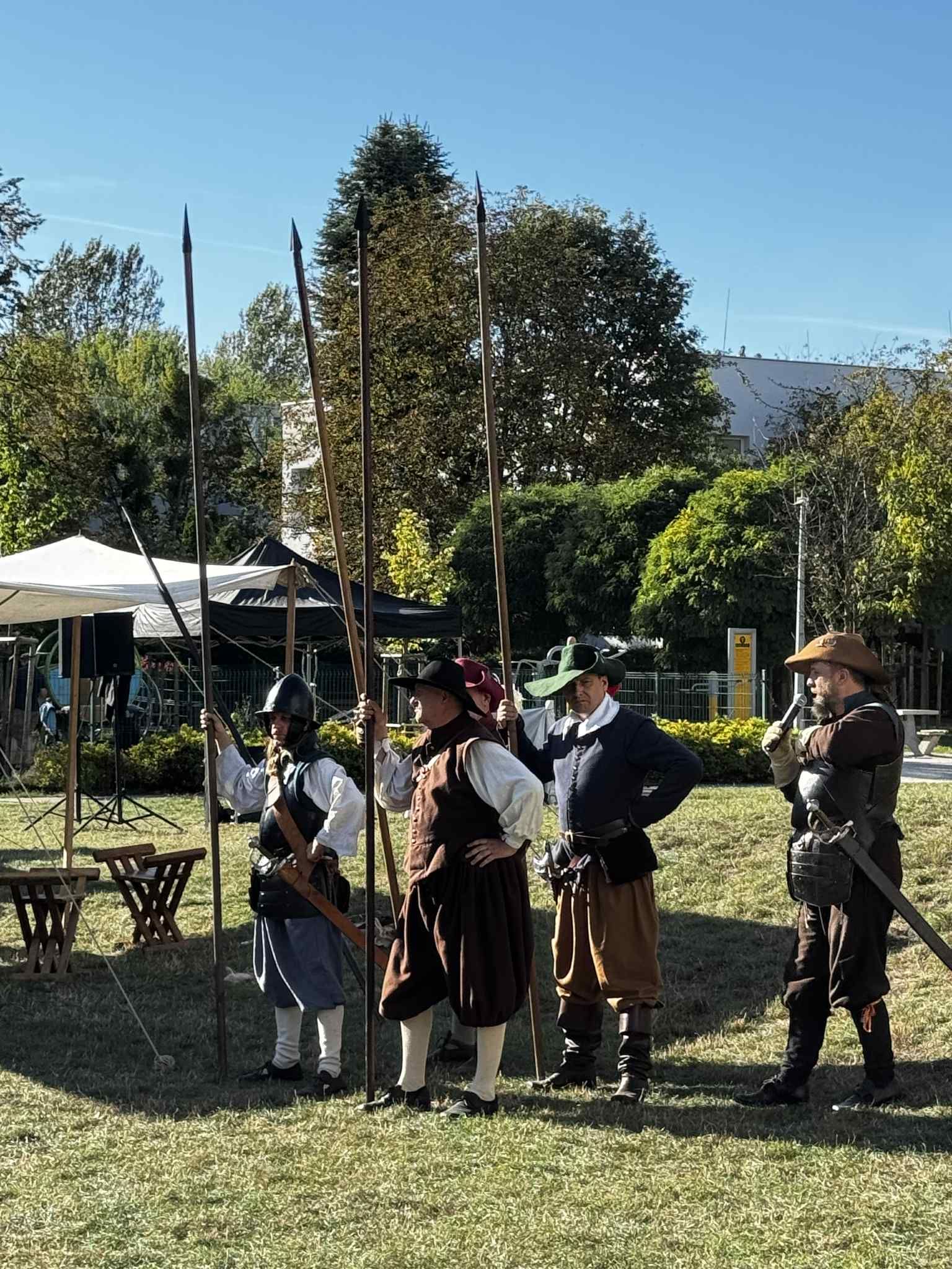 bbb862a4-4442-45d7-a6b0-0db40a0473b1 Czterech mężczyzn ubranych w stroje historyczne prezentuje pokaz z włóczniami podczas pikniku