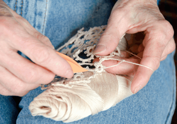 Zbliżenie na dłonie osoby wykonującej koronkę frywolitkową przy użyciu czółenka i nici.