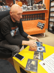 Mężczyzna siedzi na krześle przy stole, na którym leżą płyty muzyczne.