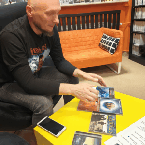 Mężczyzna siedzi na krześle przy stole, na którym leżą płyty muzyczne.