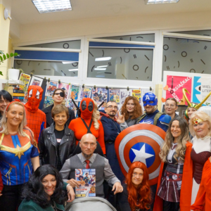 Grupa osób przebranych za superbohaterów, uśmiechniętych i pozujących do zdjęcia w kolorowych kostiumach.