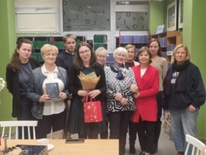 Grupa ludzi stoi wokół stołu, trzymając książki w rękach.