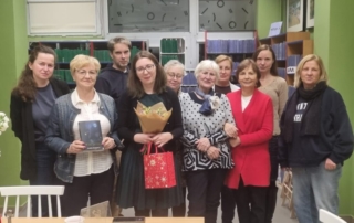 Grupa ludzi stoi wokół stołu, trzymając książki w rękach.