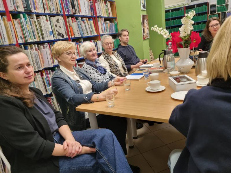 image000002_1764143886643 Uczestnicy spotkania siedzą przy stole w bibliotece, z książkami i notatkami przed sobą.