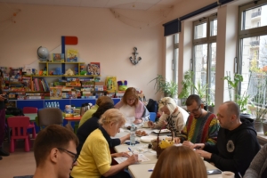 Grupa ludzi siedzi przy stole, jedząc i prowadząc wywiad.