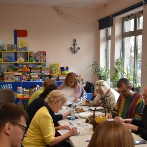 Grupa ludzi siedzi przy stole, jedząc i prowadząc wywiad.