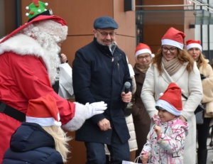 Święty Mikołaj z dziećmi, otoczeni radosnymi ludźmi w czapkach Mikołaja, wszyscy uśmiechnięci