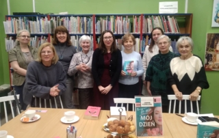 Grupa kobiet stoi wokół stołu z książkami, rozmawiając i przeglądając materiały