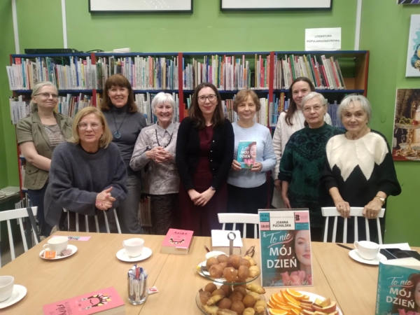 Grupa kobiet stoi wokół stołu z książkami, rozmawiając i przeglądając materiały