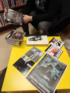 Mężczyzna siedzi przy żółtym stole, obok niego leży stos książek.