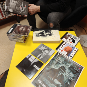 Mężczyzna siedzi przy żółtym stole, obok niego leży stos książek.