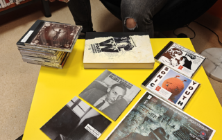 Mężczyzna siedzi przy żółtym stole, obok niego leży stos książek.