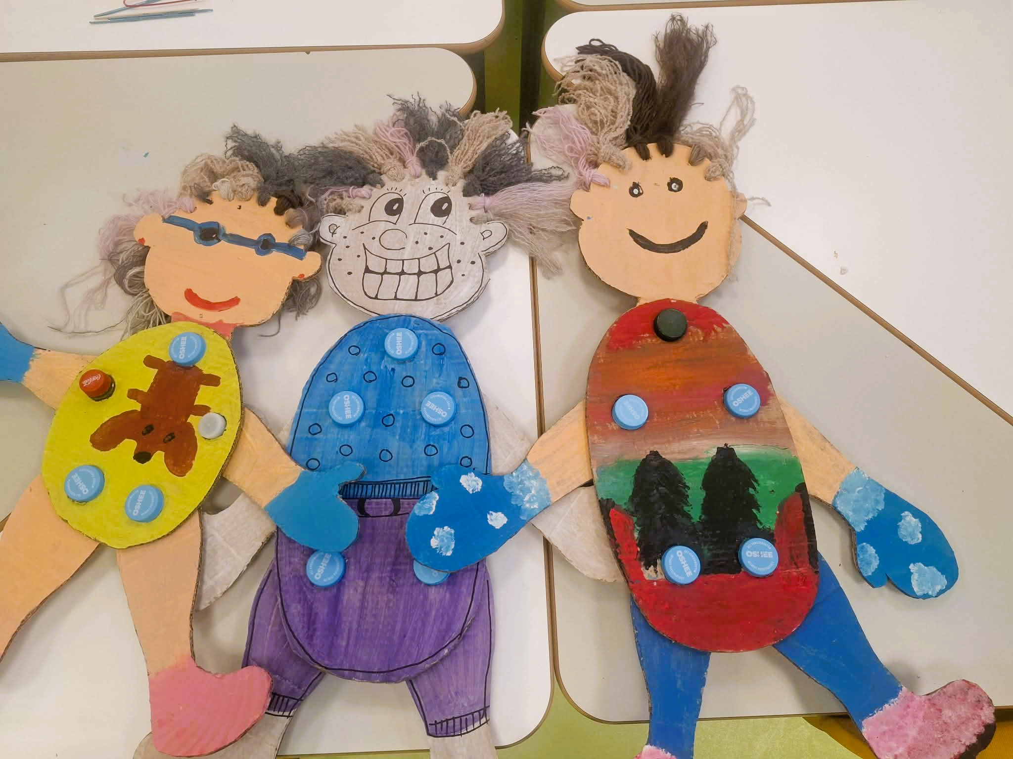 Biblioteka. (3) Trzy kolorowe papierowe ludziki z ubraniami, zrobione z kartonu, przedstawione na jasnym tle.