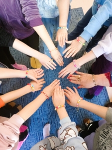 Dzieci w kręgu trzymają się za ręce, pokazując swoje bransoletki.