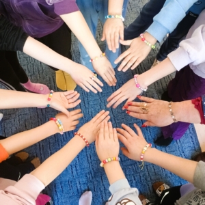 Dzieci w kręgu trzymają się za ręce, pokazując swoje bransoletki.