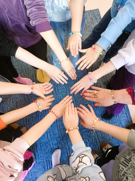 Biblioteka. (4) Dzieci w kręgu trzymają się za ręce, pokazując swoje bransoletki.