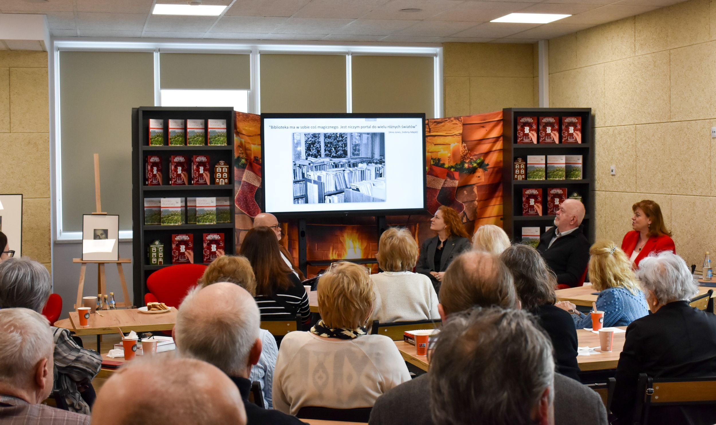 DSC_2028 Grupa ludzi siedzących przy stolikach słucha brunetki w ciemnym kostiumie przemawiającej przez mikrofon w obecności stojących obok niej trzech pań