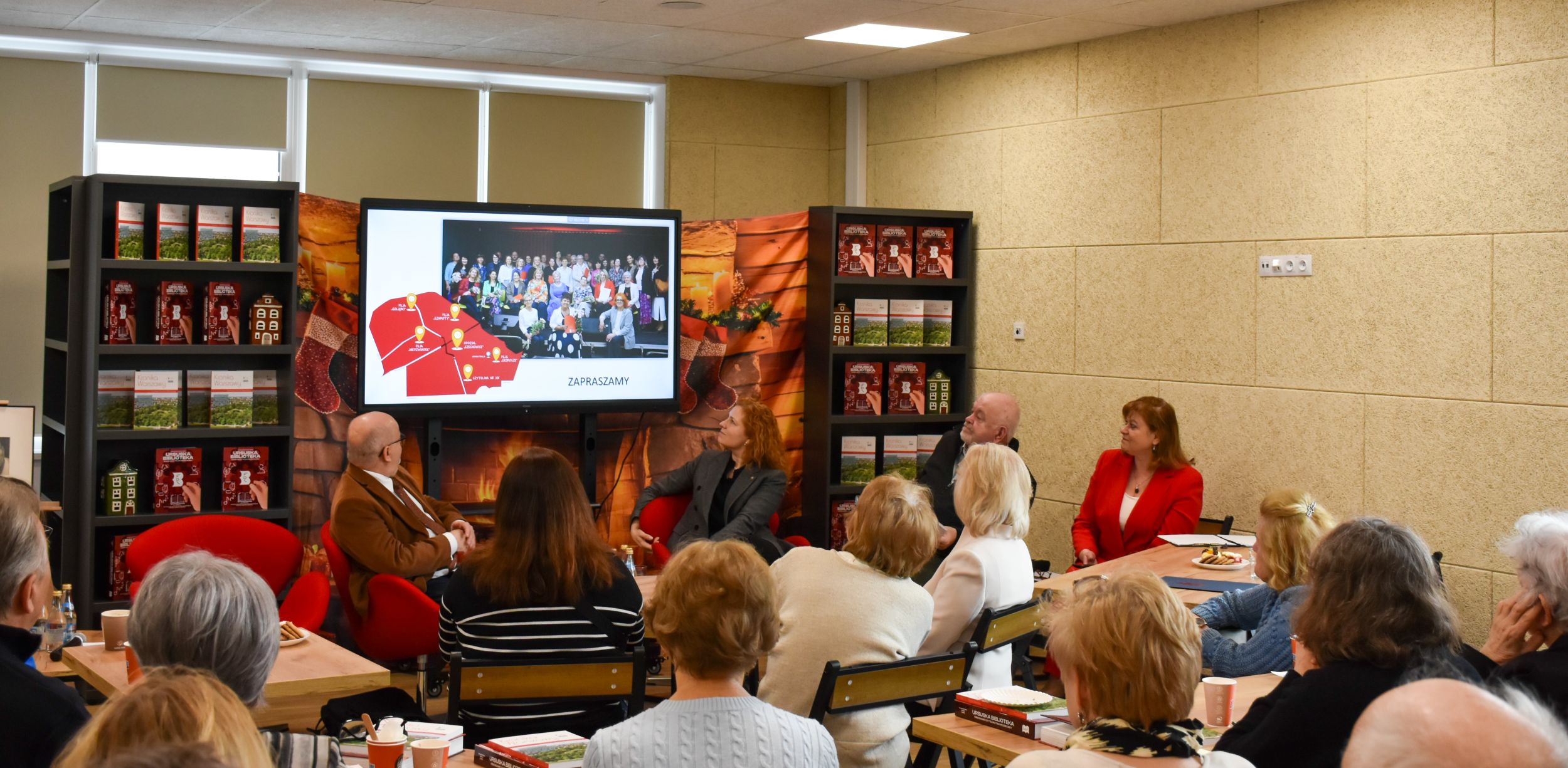 DSC_2044 Grupa uśmiechniętych siedzących przy stolikach ludzi ogląda pokaz slajdów na tablicy