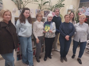 Widzimy grupę ludzi przed półką z książkami, którzy uśmiechają się