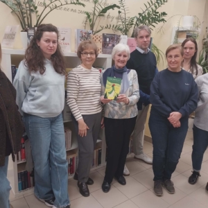 Widzimy grupę ludzi przed półką z książkami, którzy uśmiechają się