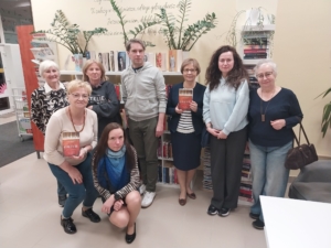 Widzimy grupę ludzi przed półką z książkami, którzy uśmiechają się