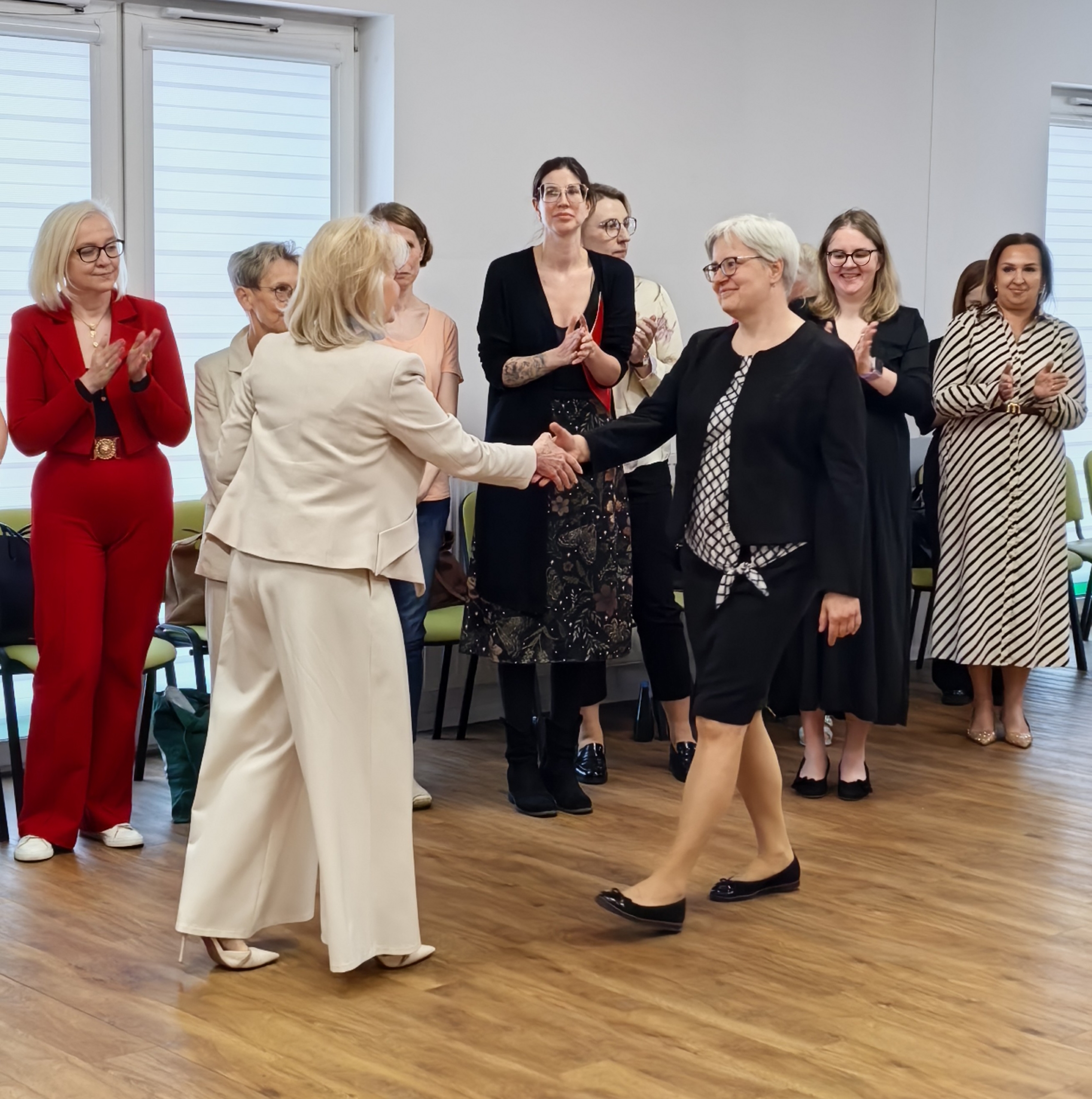_cuva Jedna kobieta wyciąga dłoń do drugiej. W tle stoją inne kobiety.