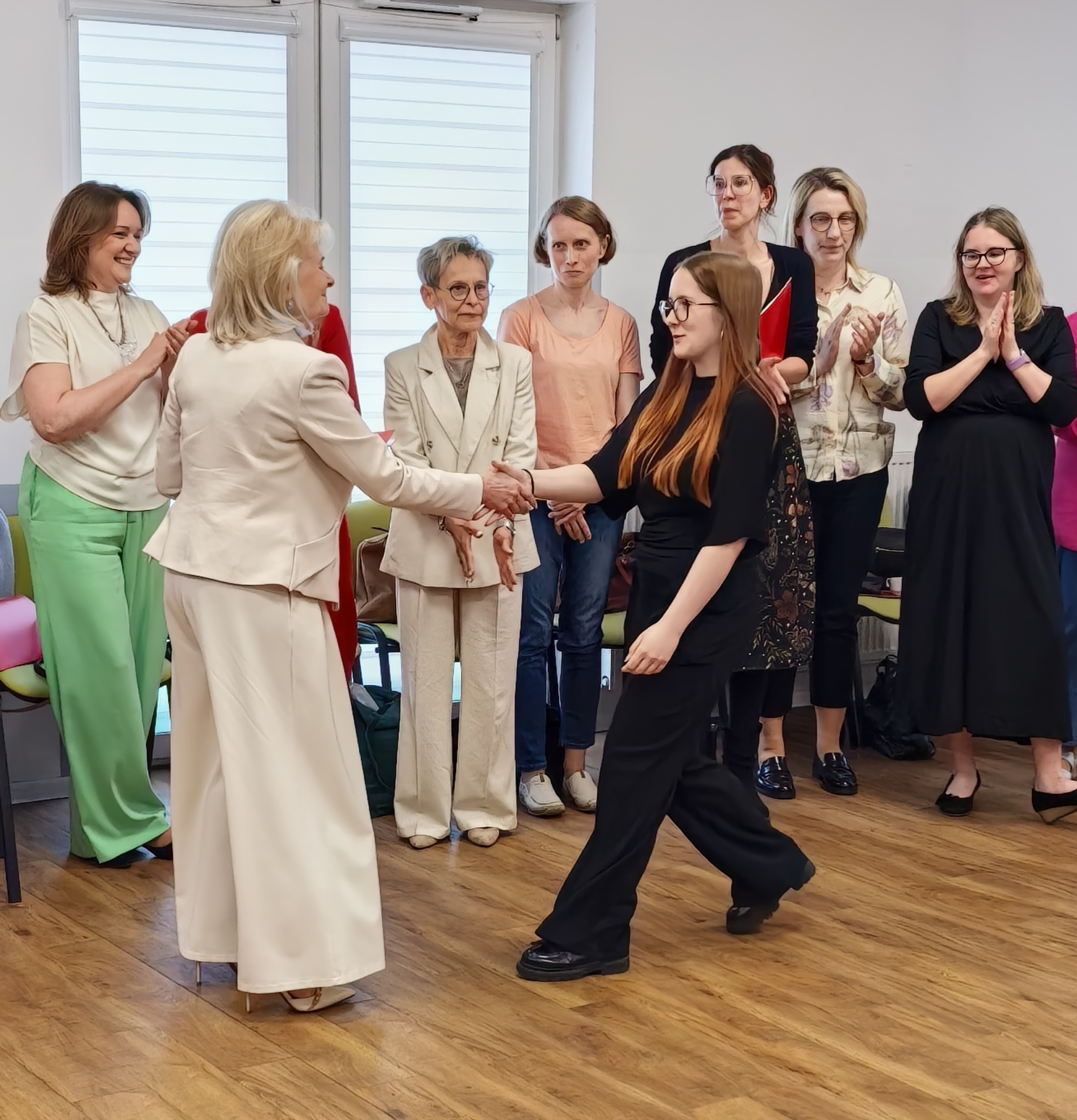 _cuva Jedna kobieta uściska dłoń drugiej. W tle - grupa innych kobiet.