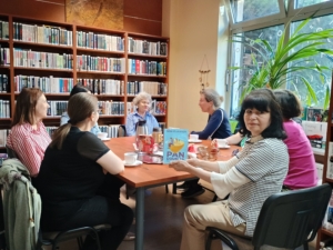 Grupa kobiet siedzących przy stole w bibliotece, prowadzących dyskusję i przeglądających książki.
