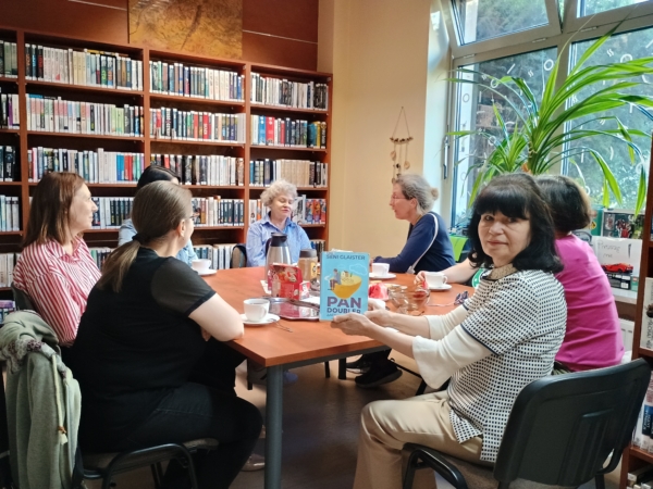 1000032037 (002) Grupa kobiet siedzących przy stole w bibliotece, prowadzących dyskusję i przeglądających książki.