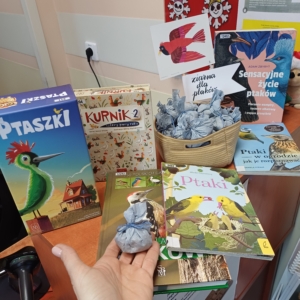 Książki dziecięce oraz koszyczek z pakiecikami ziaren dla ptaków.