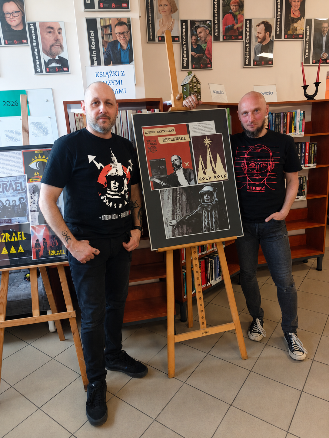 DKM_2 Dwaj mężczyźni stoją obok plakatu w bibliotece.