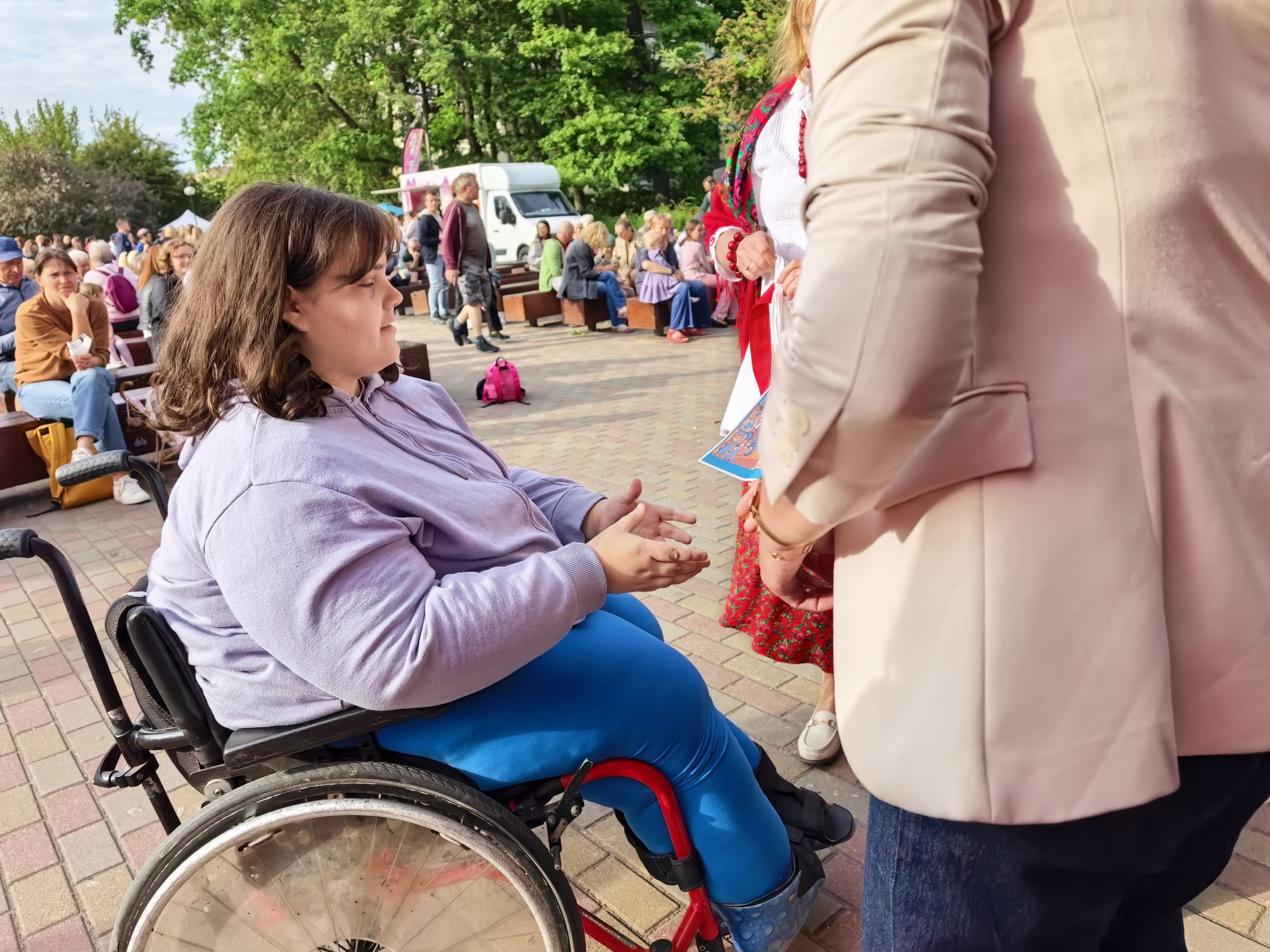 _cuva Kobieta na wózku inwalidzkim otrzymuje prezent od uśmiechniętej osoby stojącej obok niej.