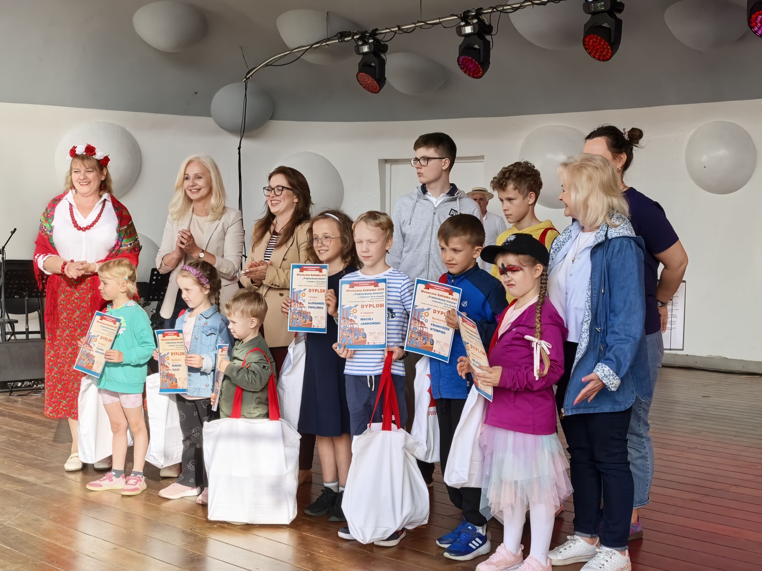_cuva Dzieci i dorośli uśmiechają się na scenie, trzymając nagrody od biblioteki, pozując do wspólnego zdjęcia.