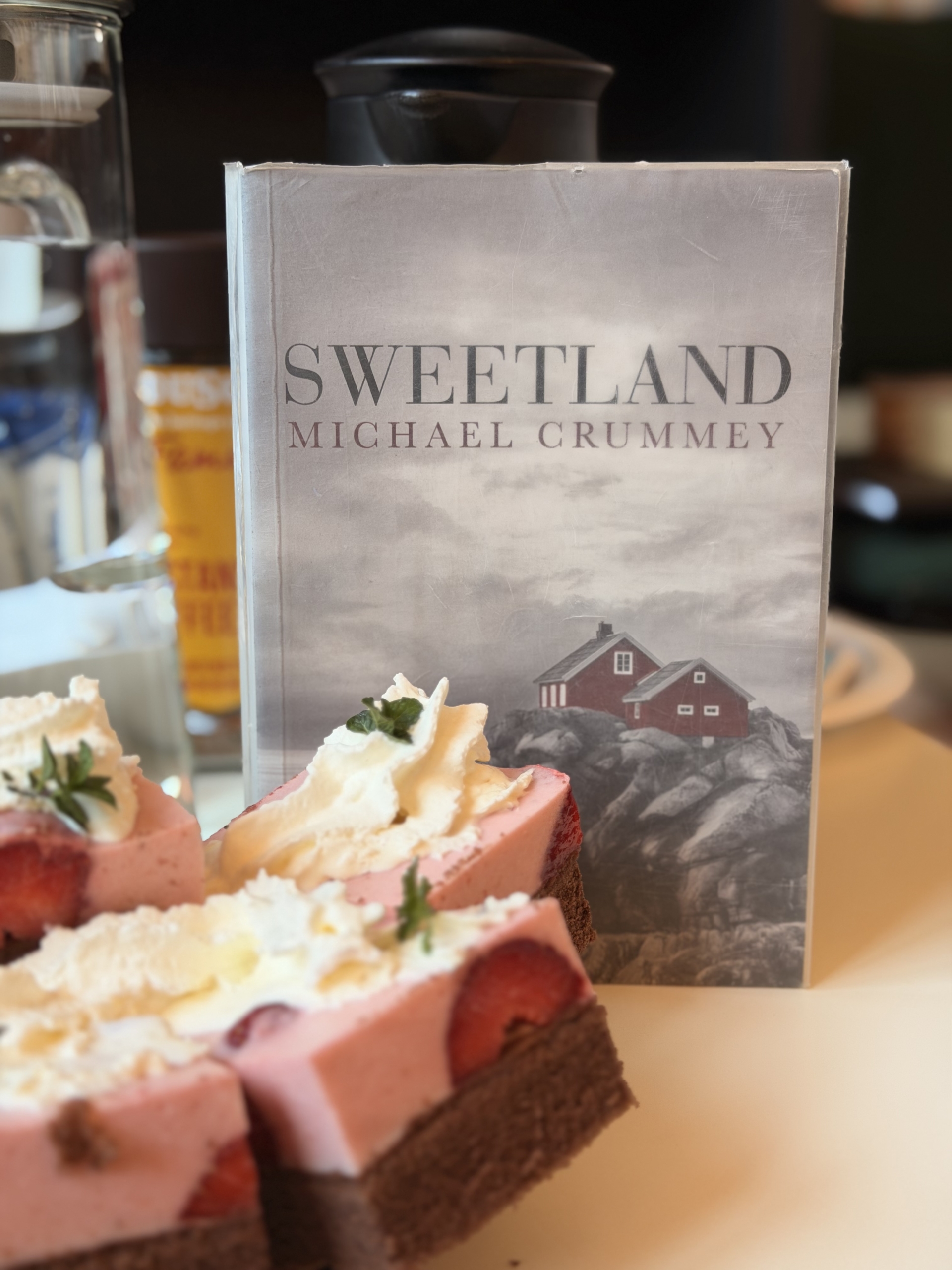 IMG_4168 Okładka książki "Sweetland" Michaela Cromleya leży na stole, obok niej znajdują się ciastka.