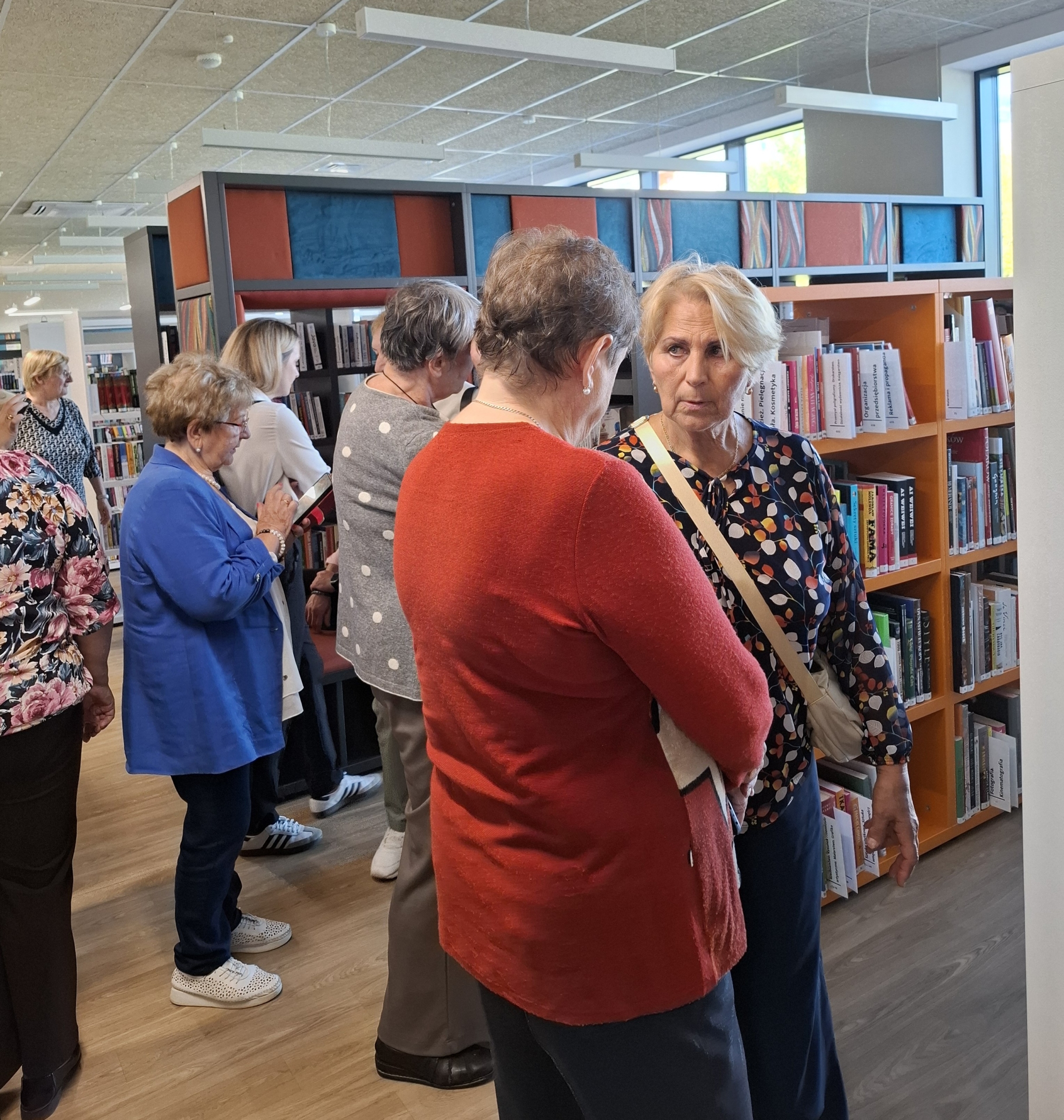 20260928_141857 Ludzie stoją w bibliotece, przeglądając książki na półkach.
