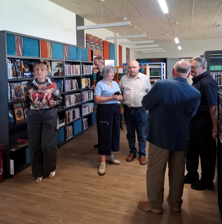20260928_141946 Ludzie stoją w bibliotece, przeglądając książki na półkach.