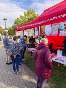 Grupka osób przed czerwonym namiotem z kolorowymi plakatami zawieszonymi pod jego dachem.