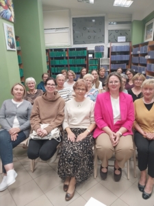 Grupa kobiet w bibliotece, uśmiechających się do kamery wśród regałów z książkami.