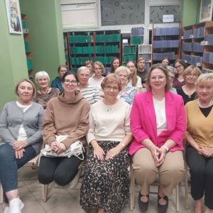 Grupa kobiet w bibliotece, uśmiechających się do kamery wśród regałów z książkami.